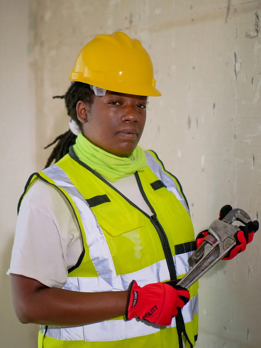 A worker in protective gear holding a pipe wrench